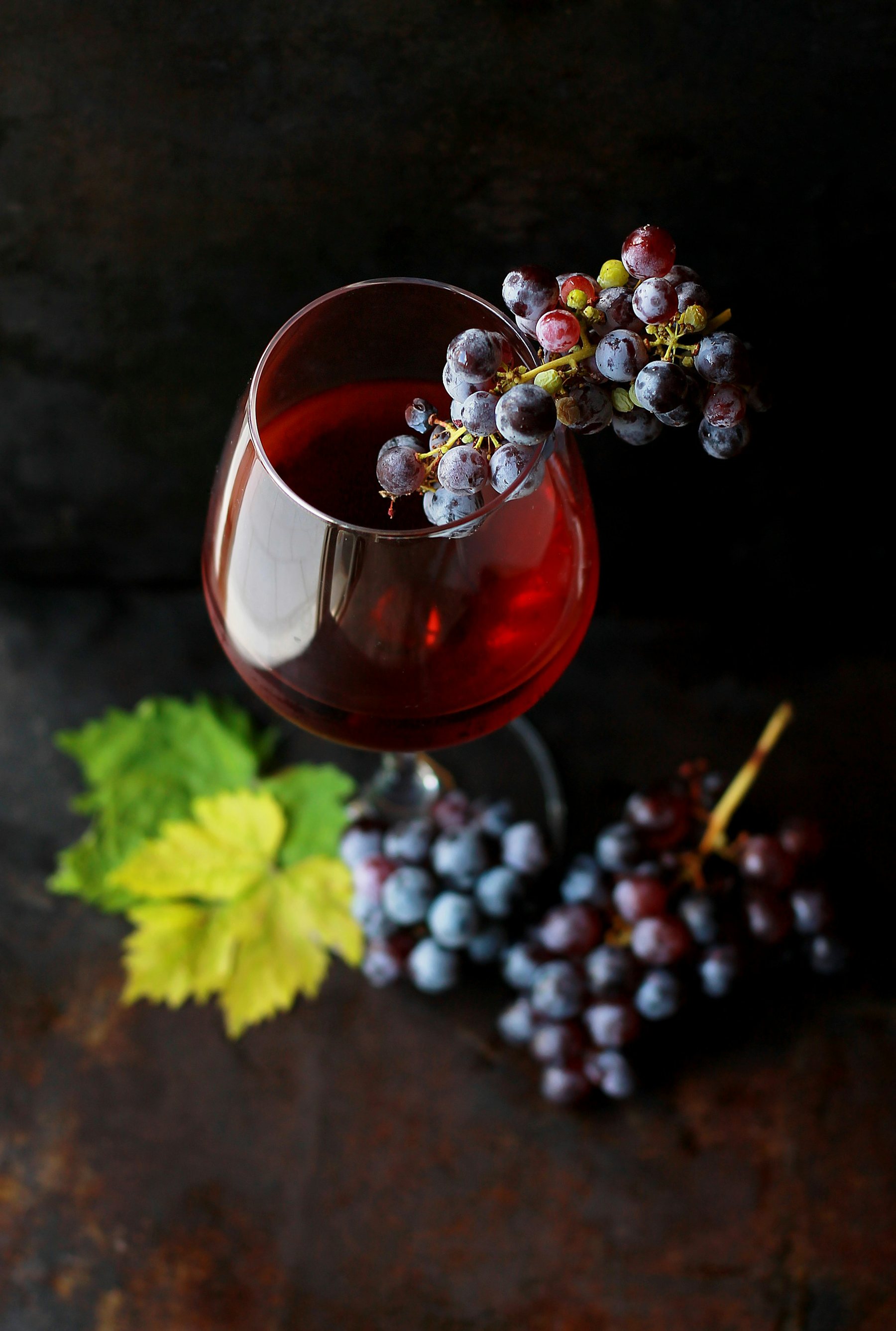 Crystal glass of fine red wine with grapes in low light